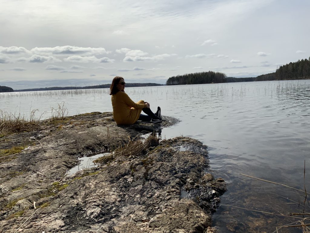 nainen istuu rantakivellä ja katsoo järvelle